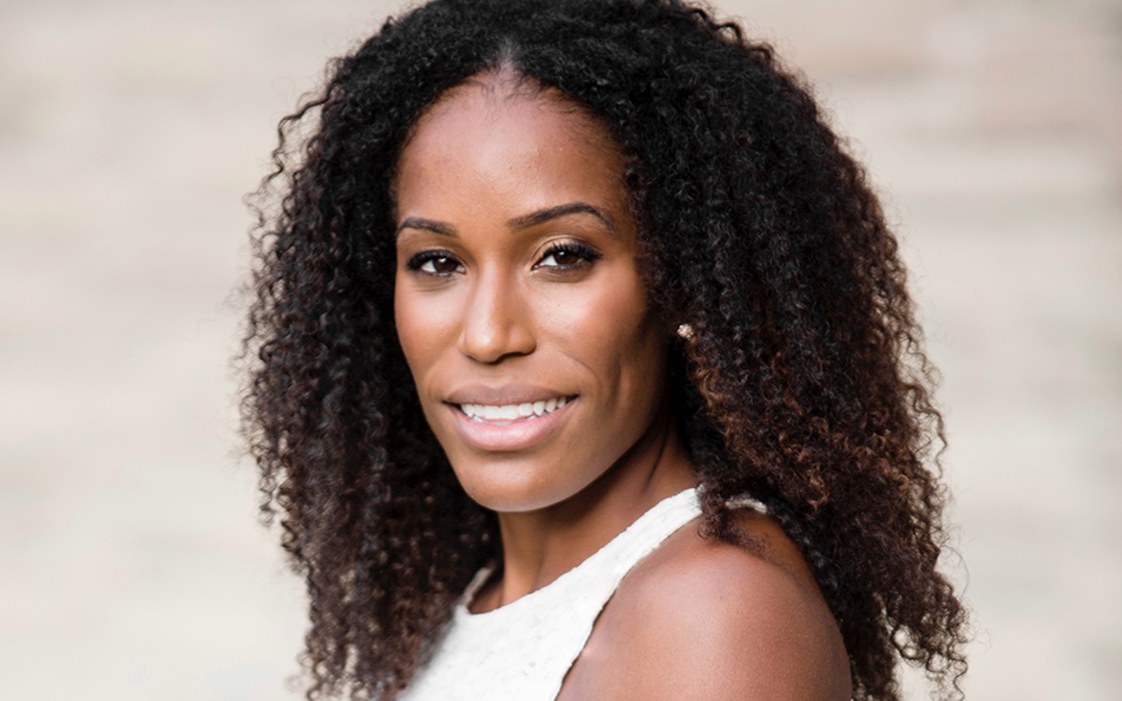 Headshot of a women with black very curly hair in a white dress. 