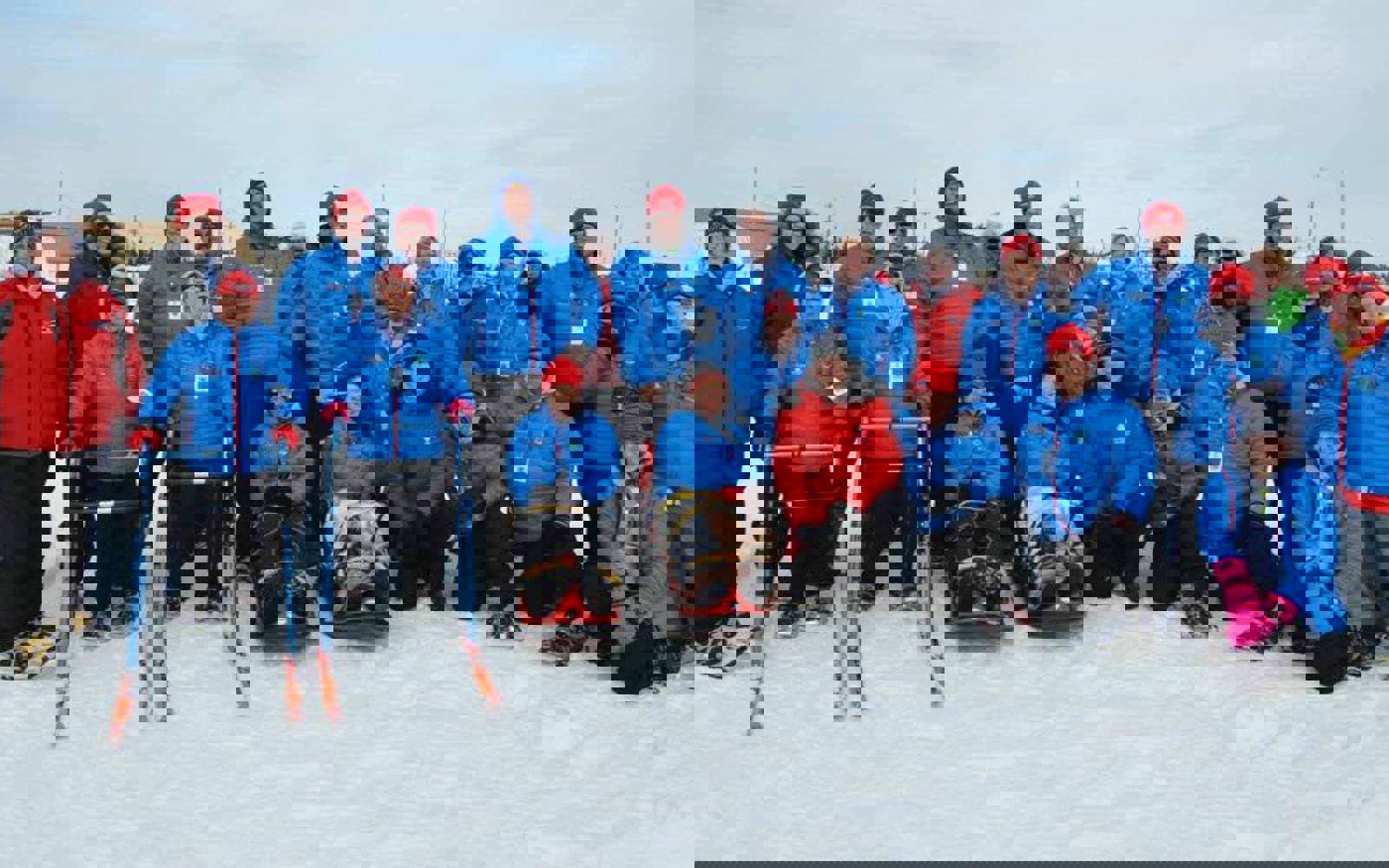 A large group photo of a Special Olympics Newfoundland & Labrador team. They are all wearing blue puffer jackets and some are additionally wearing red toques. It is wintertime and everyone is standing outside in the snow.