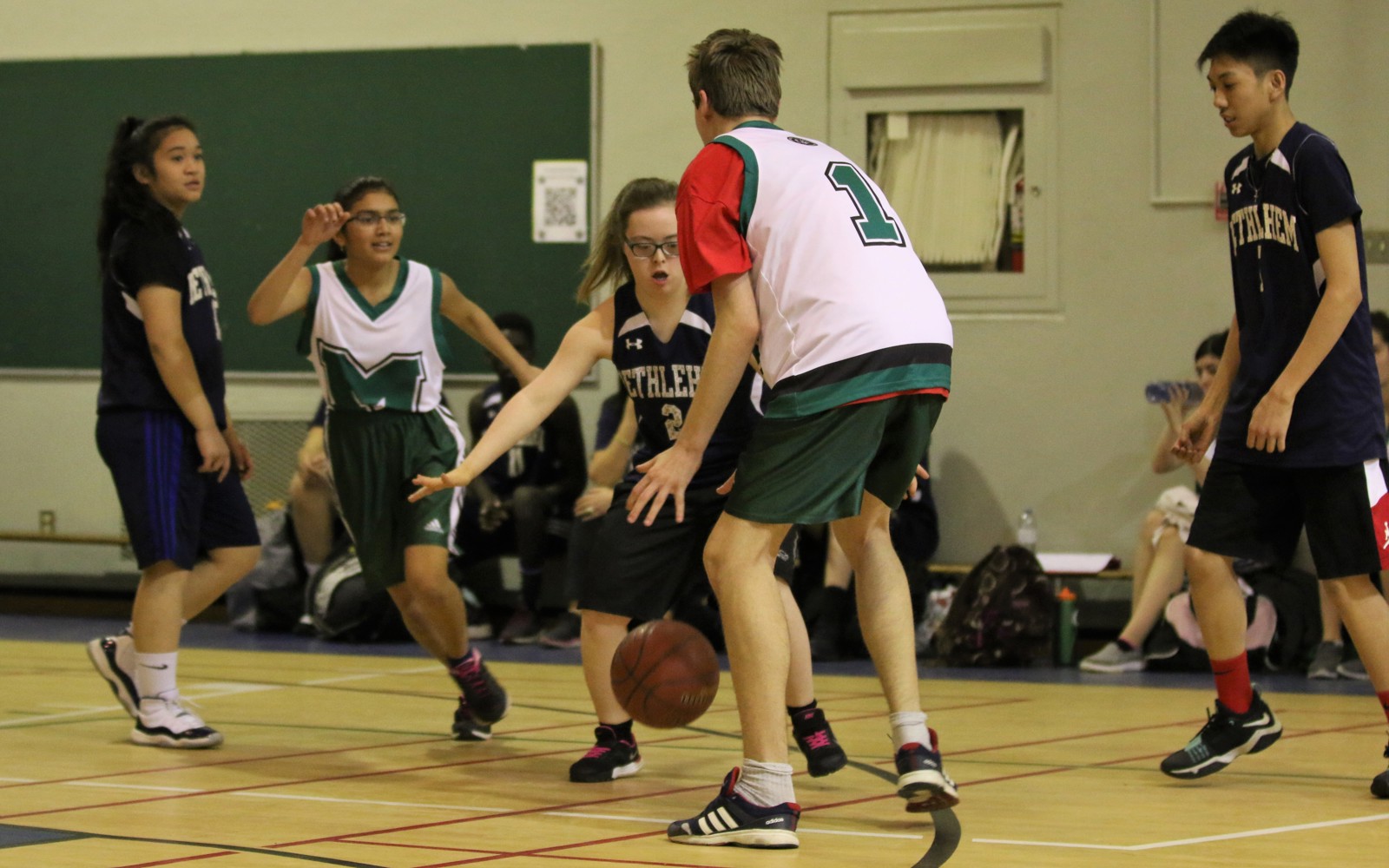 A action shot photo of a unified basketball game. Five athletes can be seen playing basketball on the court. One athlete is dribbling the ball while another is trying to defend him.