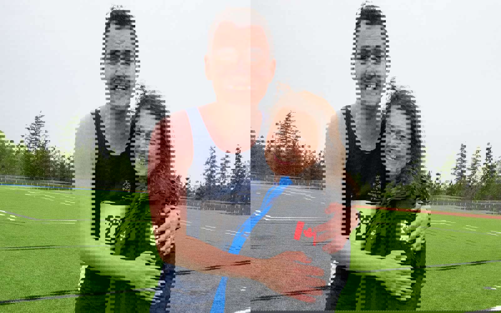 A picture of an athlete with their coach. The athlete has his arms around his coach like a hug. They are both standing and smiling for the camera.