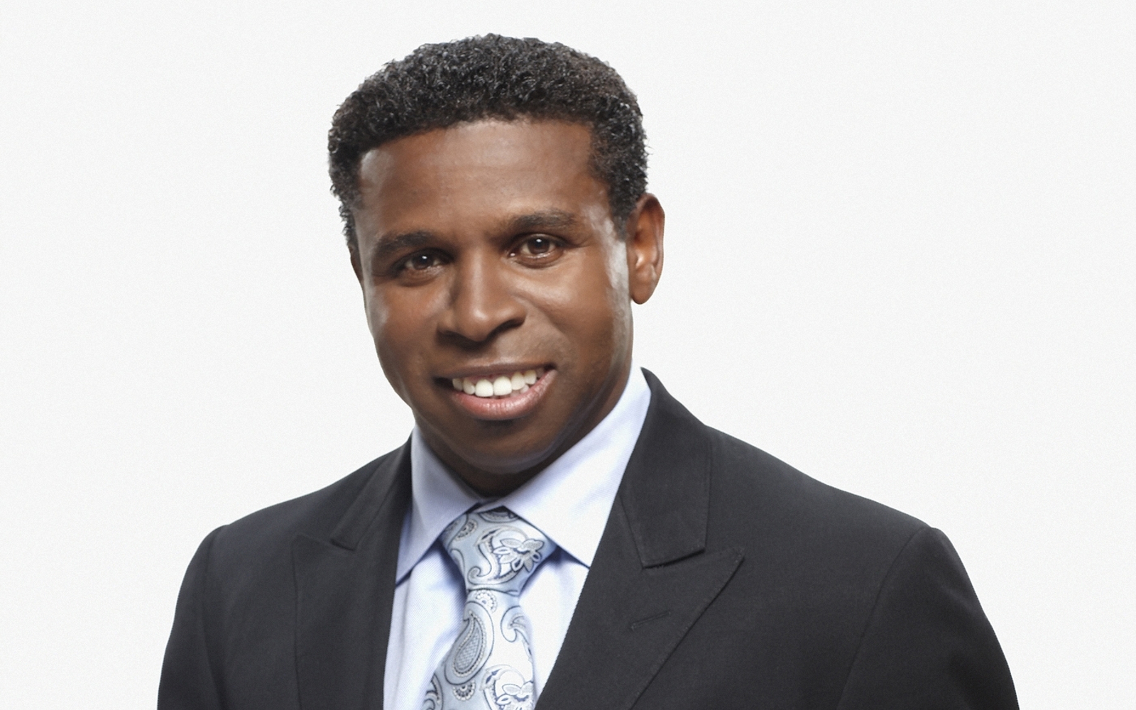 Headshot of a man in black suit and blue and white paisley tie. 
