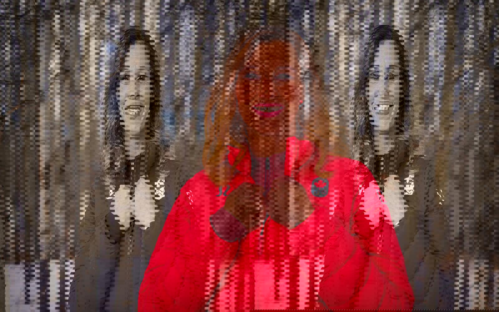 Headshot of a woman outside in the winter in a forest, wearing a red Olympics jacket. 