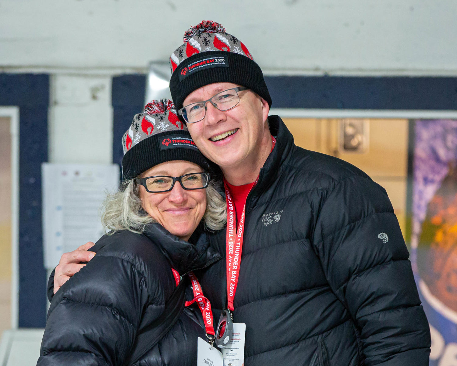 Two people in black winter jackets and Thunder Bay 2020 toques smile at the camera 