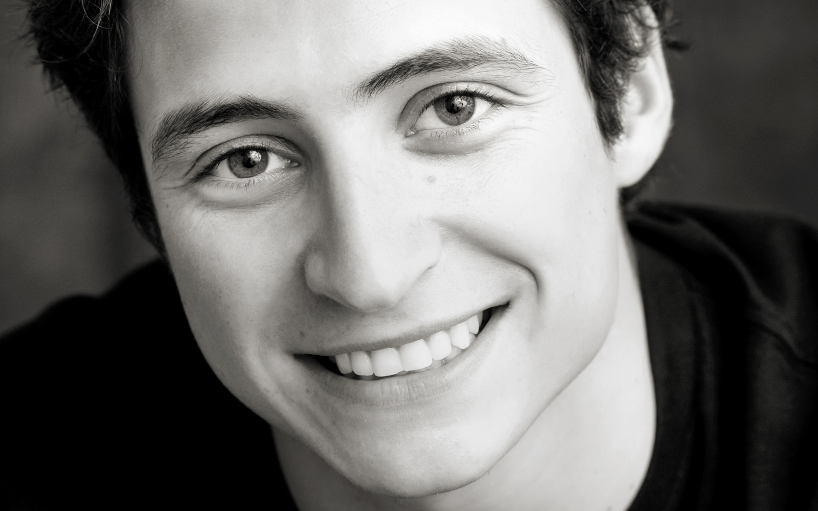 Black and white headshot of a man with dark hair and black shirt. 