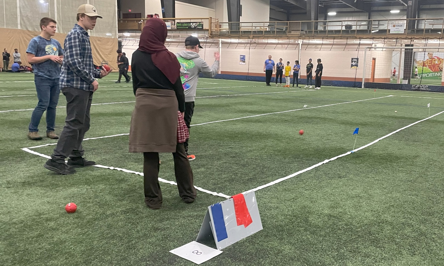 A unified sports match. Wide shot image of athletes playing bocce on a field. Four athletes are seen playing closer to the camera, while another group of athletes can be seen playing in the distance.