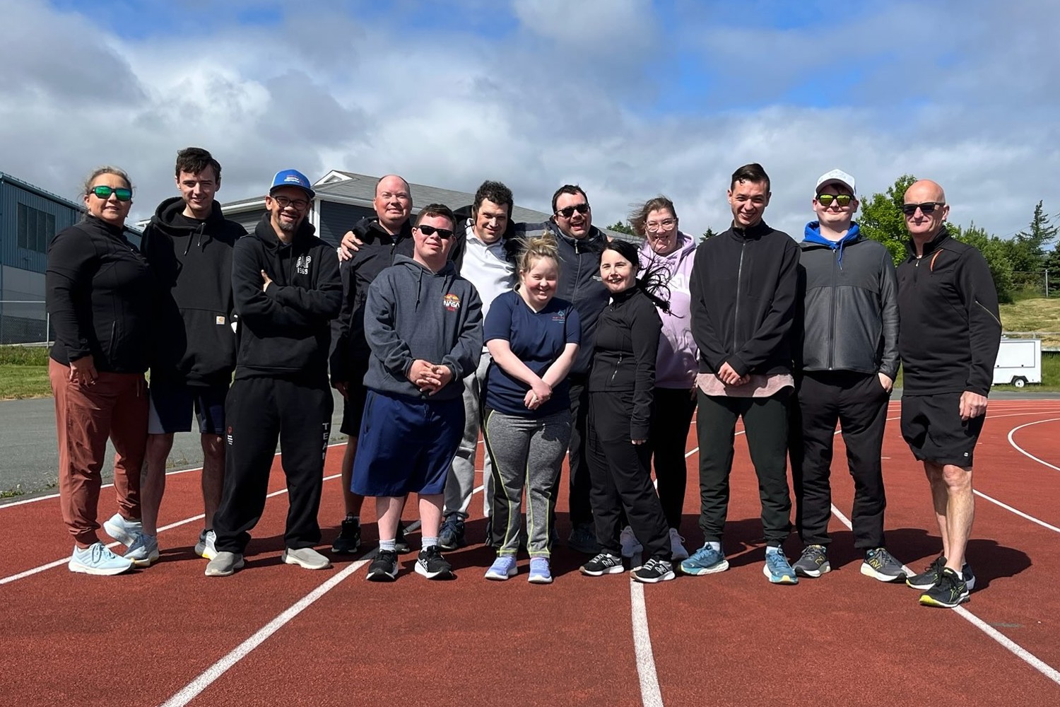 A group photo of a Special Olympics Newfoundland & Labrador team. There is 13 people in the photo and they are all standing on the track.