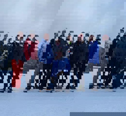 A group photo of everyone who was at the training camp. The photo takes place outside during the wintertime. Everyone is wearing winter jackets and smiling for the camera.