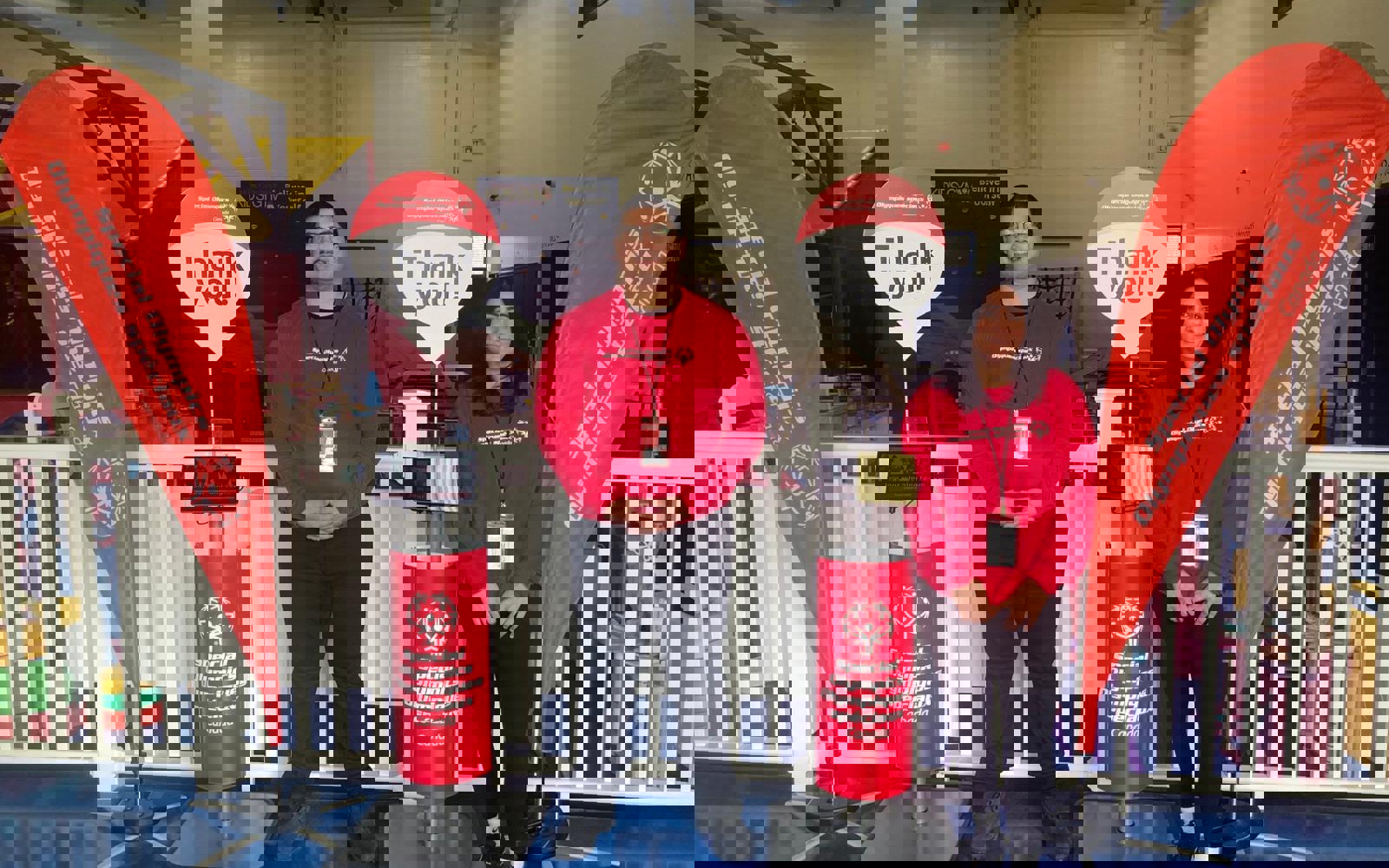 Two people in red shirts standing in front of Special Olympics signs and flags 