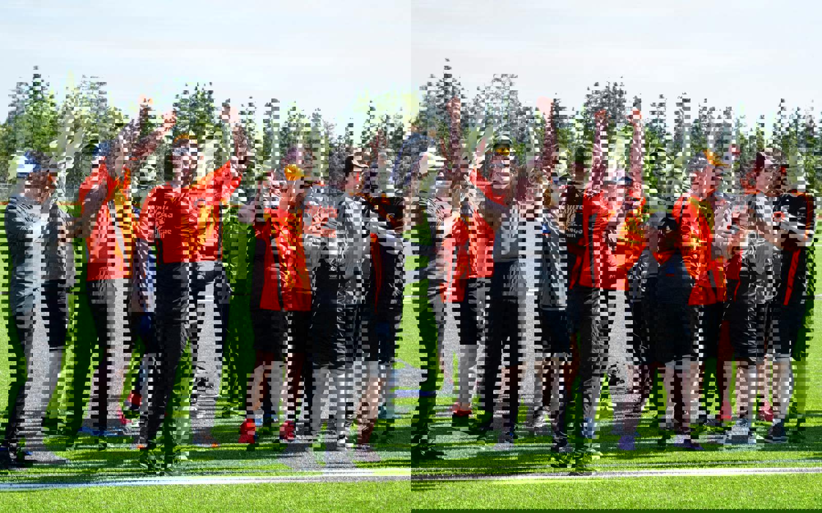 A sports team, out on the field in black and orange jerseys, with their arms up in the air cheering.