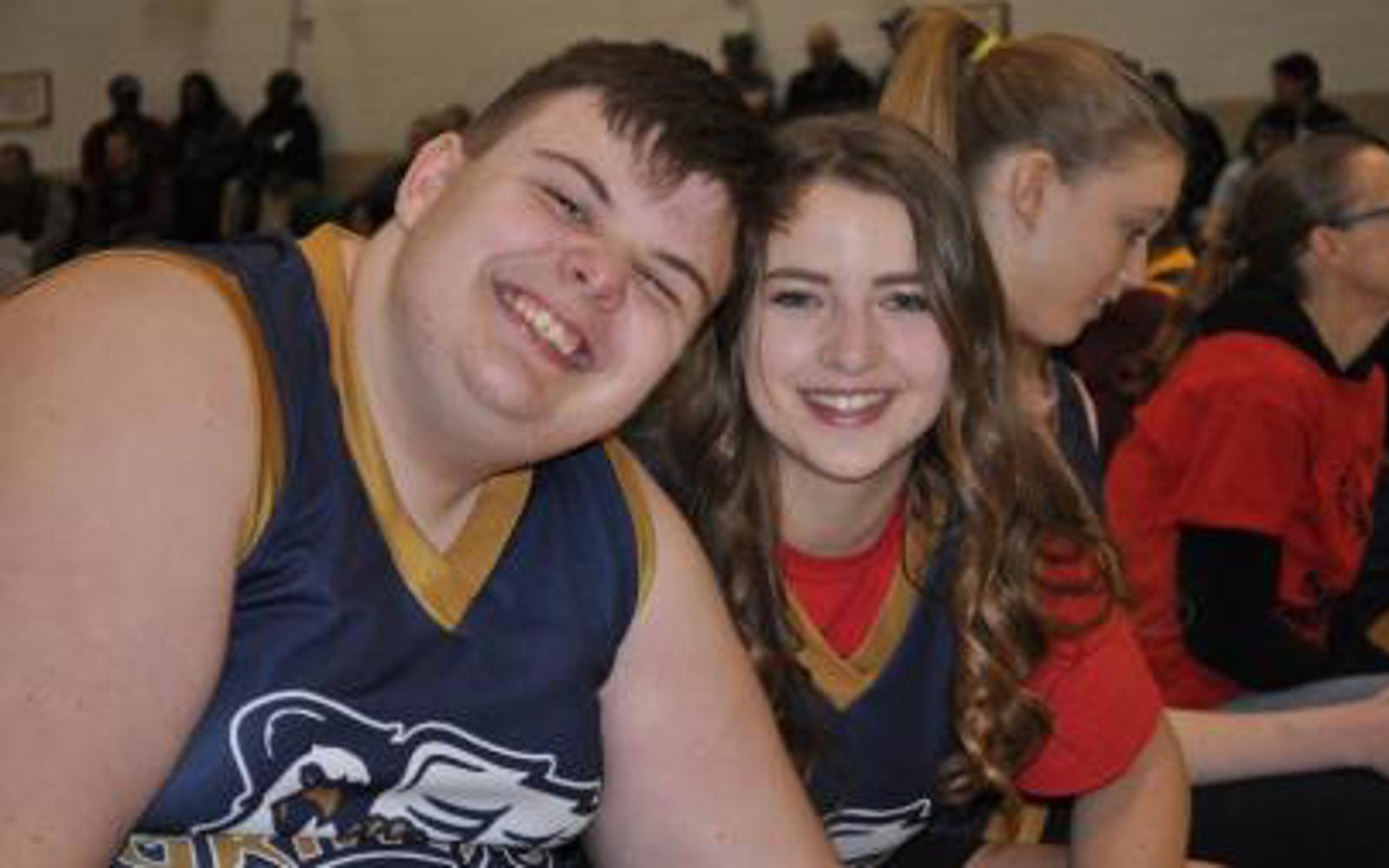 Two athletes smiling for the camera. They are wearing black and gold basketball jerseys.
