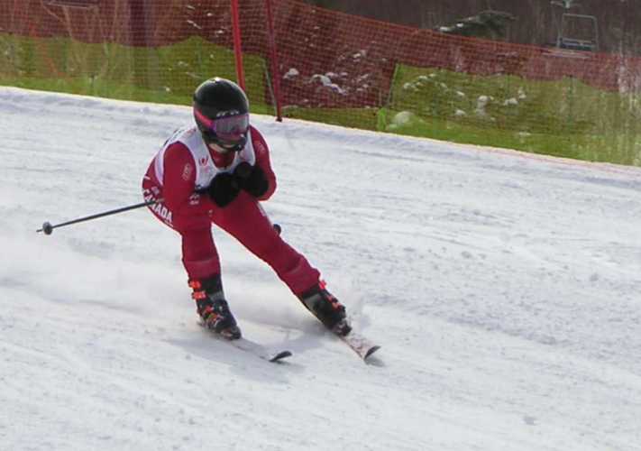 An athlete skiing down a slope. They are wearing a red skiing outfit with a black helmet and skis.