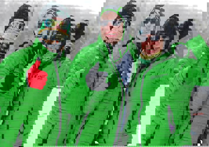 Three teammates in green Special Olympics Saskatchewan puffer jackets are smiling and giving a thumbs up to the camera.