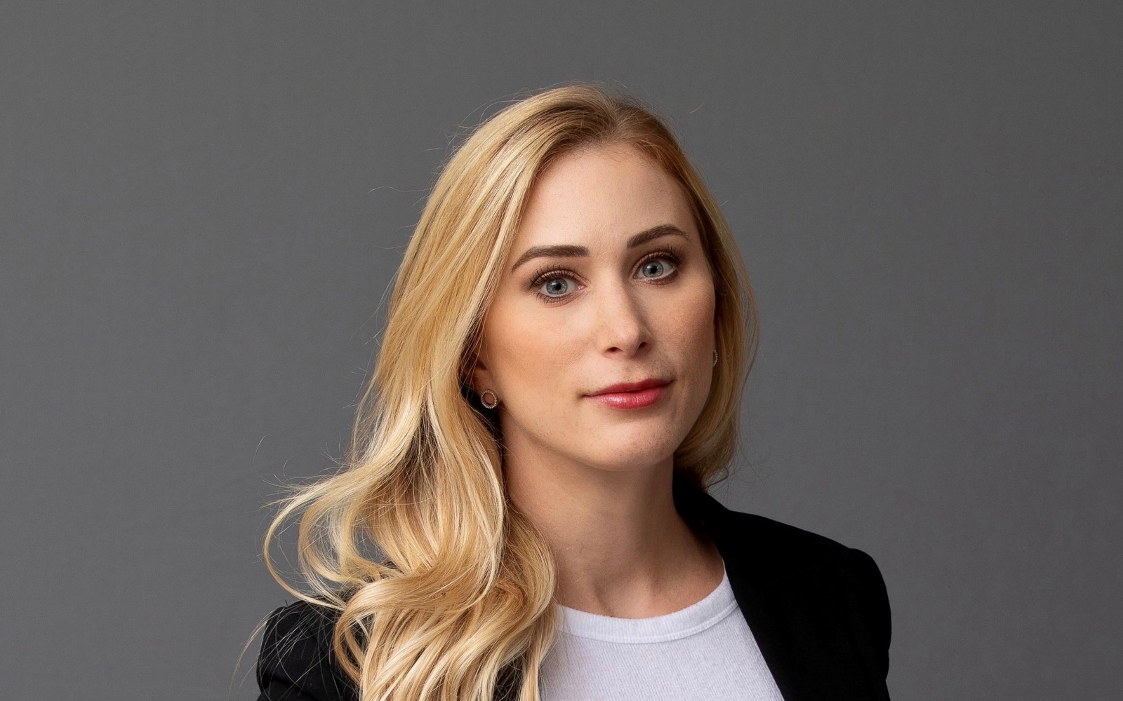 Portrait of a woman with long blond hair wearing a white sweater and a black blazer. 