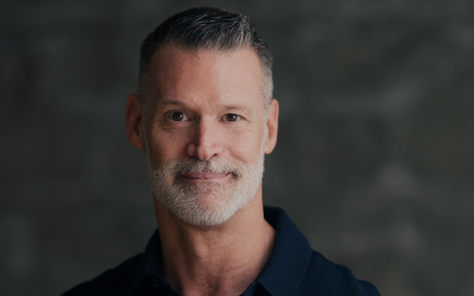 Headshot of a man in a black polo shirt. 