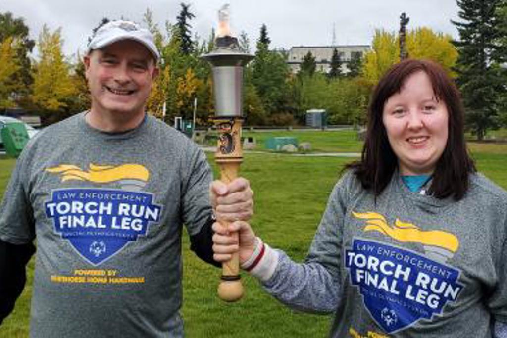 Two Law Enforcement Torch runners are smiling for the camera and holding the torch together. They are both wearing grey Law Enforcement Torch Run t-shirts.