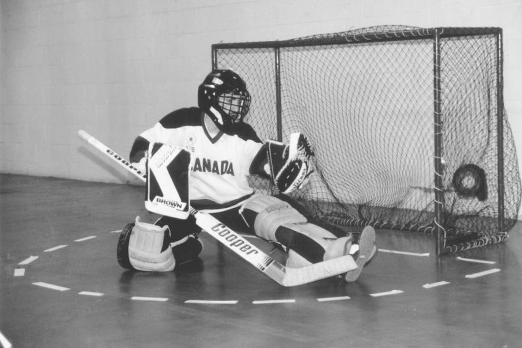 Black and white photo of a Team Canada floor hockey goalie in full gear wearing a Canada jersey, making a save against an unseen opponent