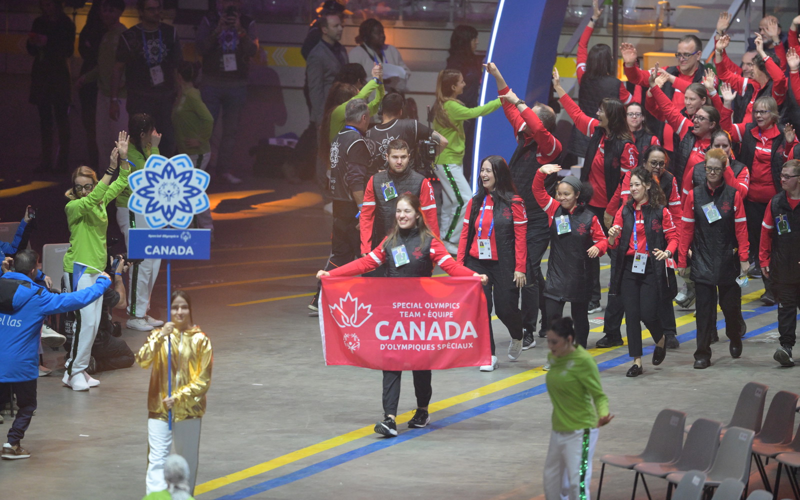 Group of athletes walking into opening ceremony. Front athlete is holding a Canadian banner with the words Special Olympics Team Canada. All athletes are dressed in red and black. 