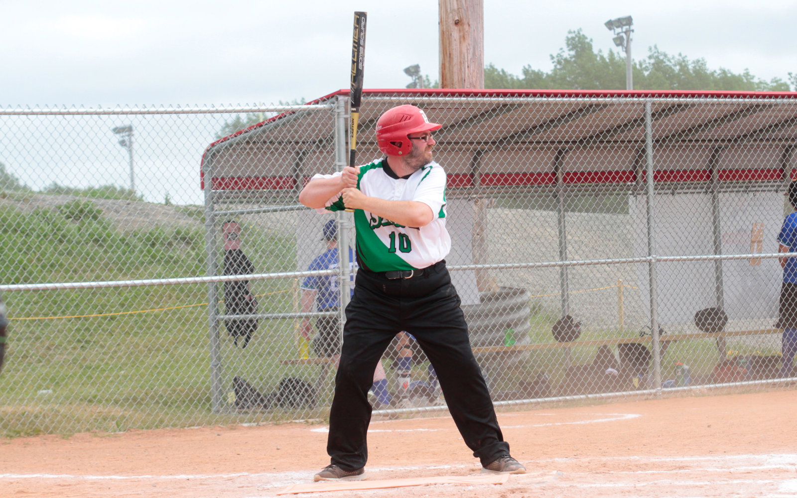 A baseball athlete at the base getting ready to hit the baseball. They are wearing a green Special Olympics Saskatchewan jersey with a red helmet. The baseball bat is swung behind their shoulder.