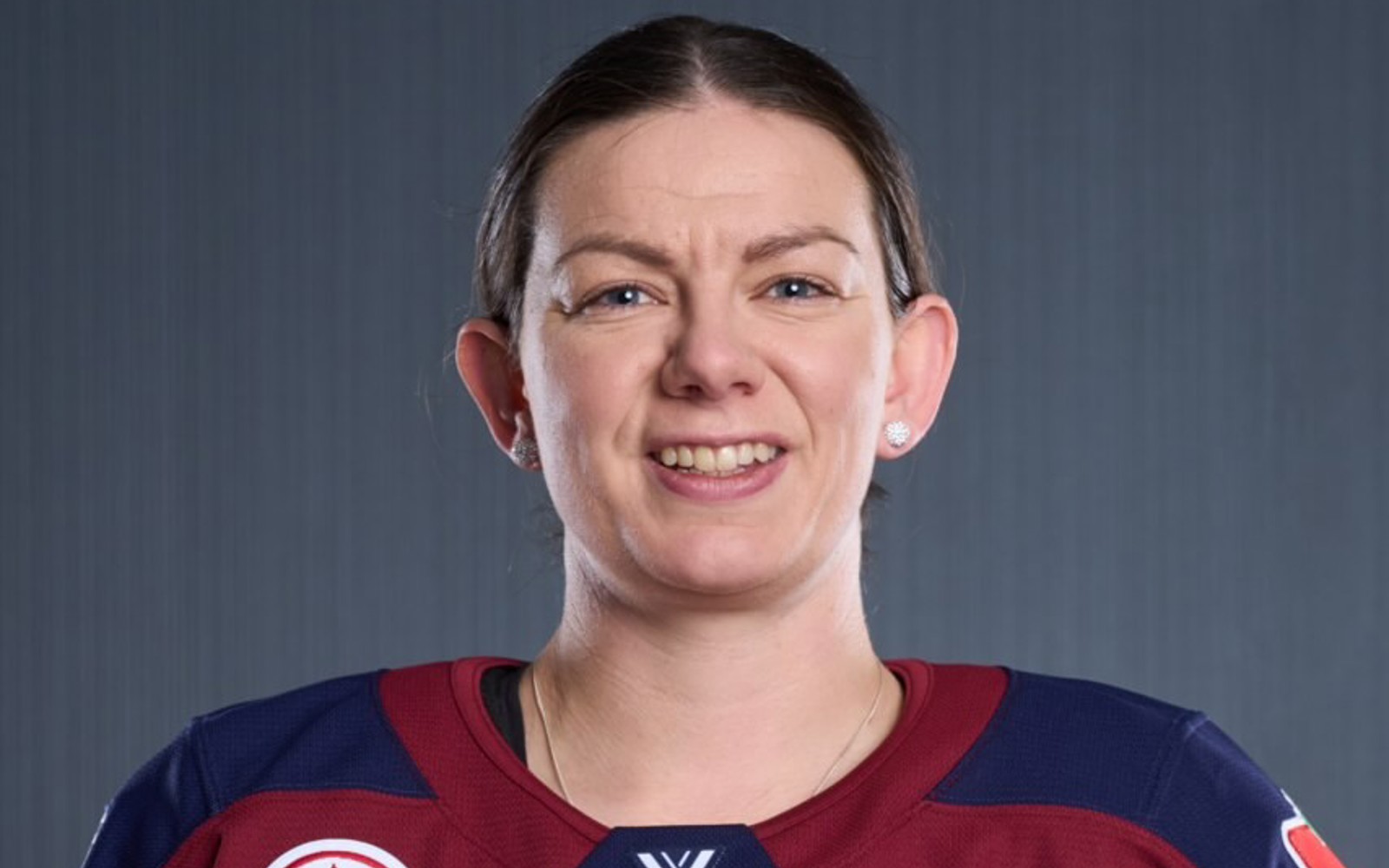 Woman wearing a hockey jersey smiling at the camera. Wearing Silver earrings. 