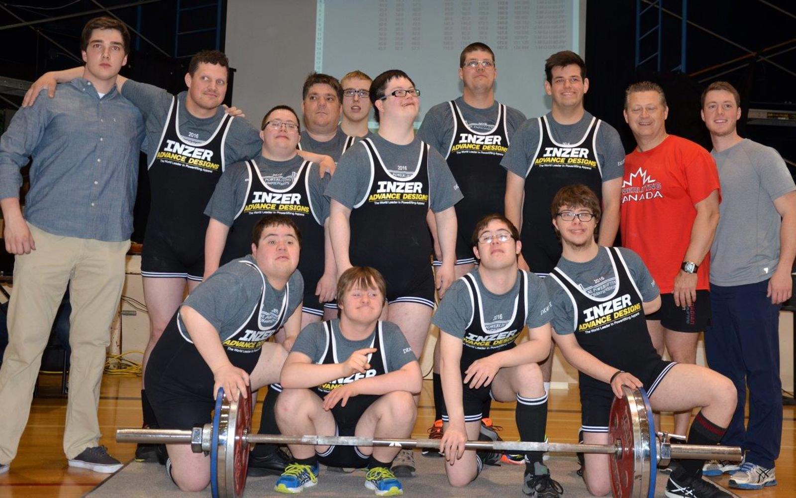 A Special Olympics Newfoundland & Labrador powerlifting team group photo. Everyone is standing in a gym in front of a large dumbbell.
