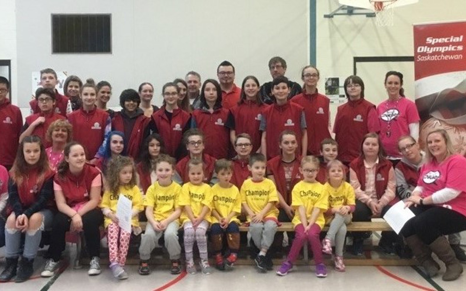 A group photo of everyone who participated in Try It! Camp. The first row is sitting on a bench while everyone else is standing. Everyone is in a gymnasium.