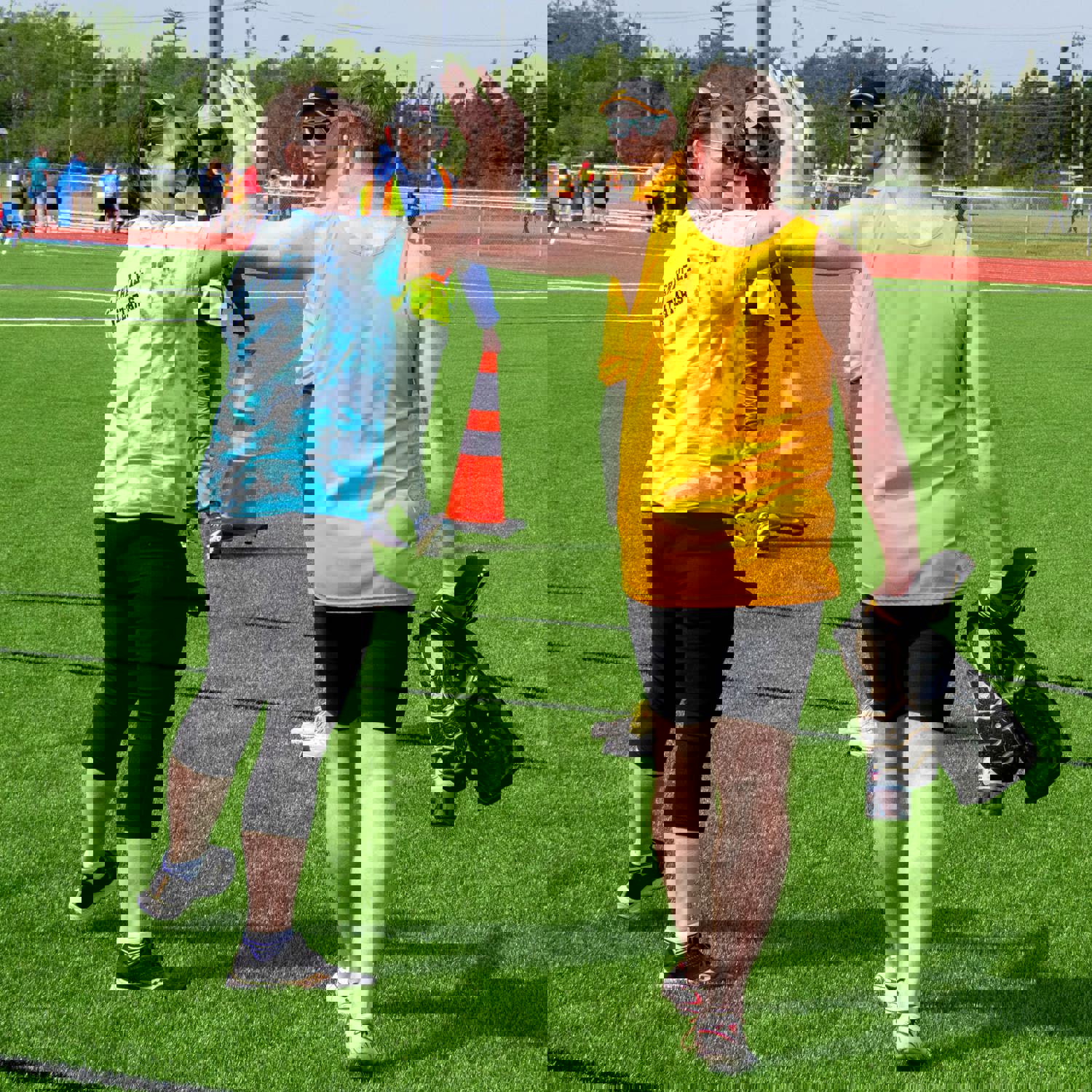 A coach is giving a high-five to an athlete. The photo was taken from behind the pair and you can only see a glimpse of the coach's face, smiling at the athlete. The athlete is holding his equipment in the hand not being used for the high five.