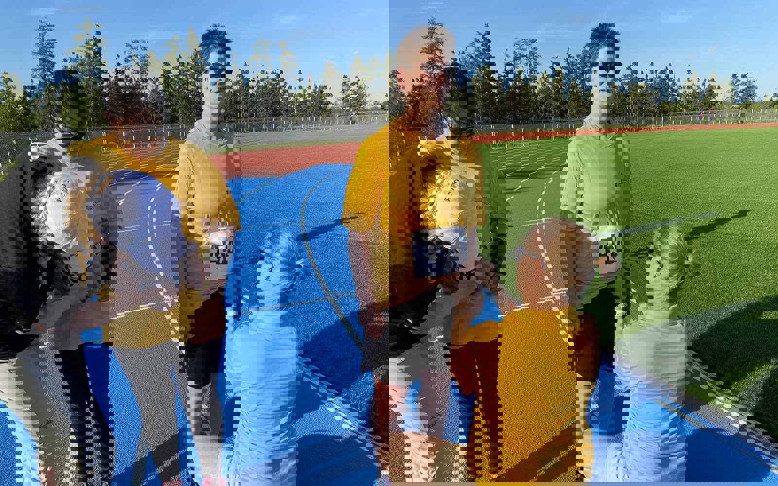 Two athletes in yellow shirts having competition bibs pinned on them by volunteers on a race track. 