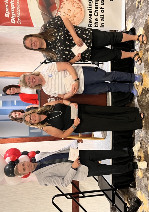 Four individuals are standing in front of a podium and holding out the awards they just won. They are smiling and posing for the camera.