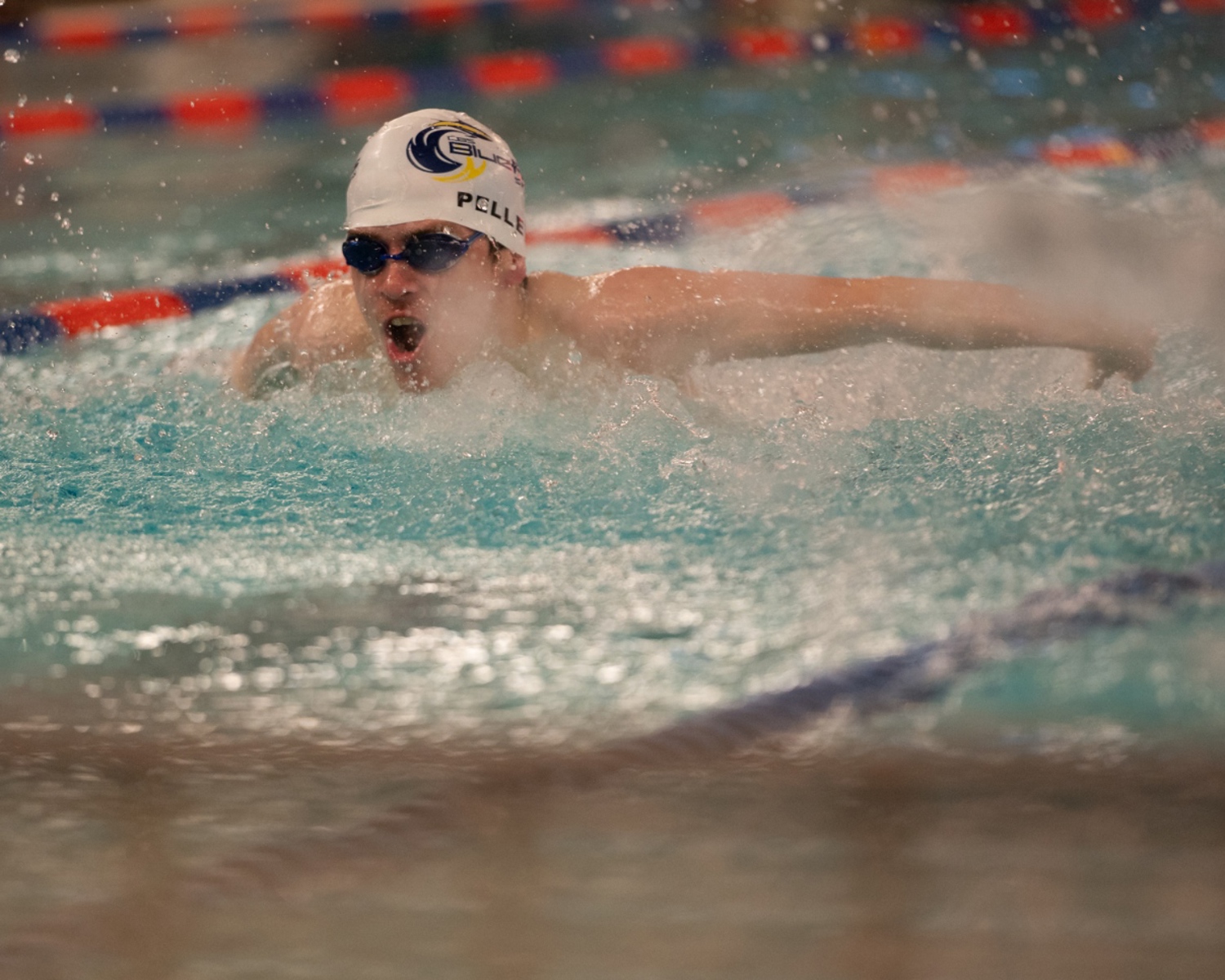 An action shot photo of a swimming athlete in the water. The athlete is wearing black goggles and a white swim cap.