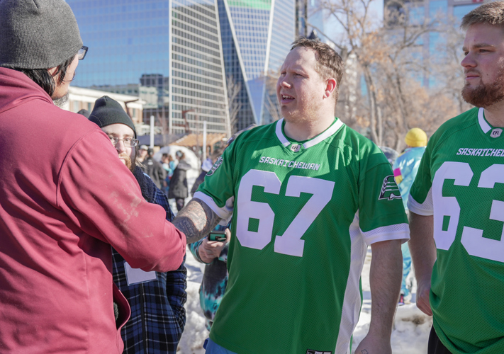 Two individuals are shaking each other's hand. One individual on the left has his back to the camera. The other individual is wearing a green "Saskatchewan" jersey with the number 67 on it and is looking at the individual he is shaking hands with..