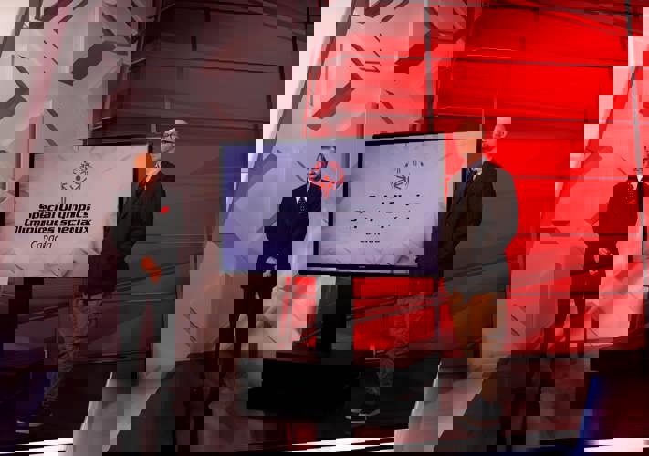 Two men standing, both are wearing suits. Between them is a TV screen with the Special Olympics Canada logo. 