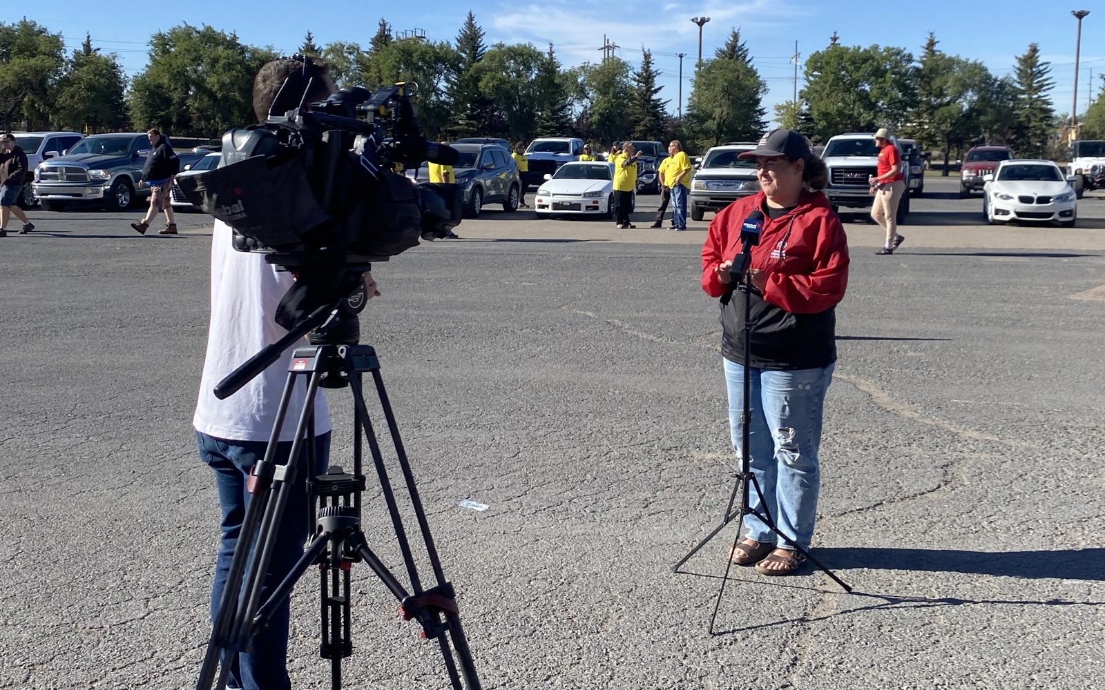 A medium shot photo of a camera on a tripod. There is an individual behind the camera, but the camera is obstructing him from view. There is also an individual in front of the camera. You can see their full body and they are wearing a red jacket with jeans.