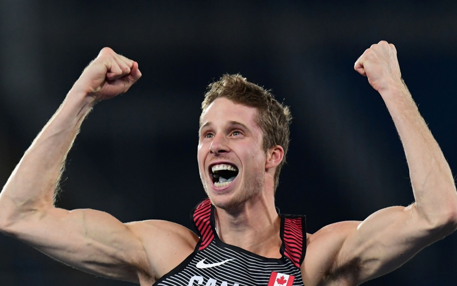 Man in an athletic tank with arms in the air cheering.