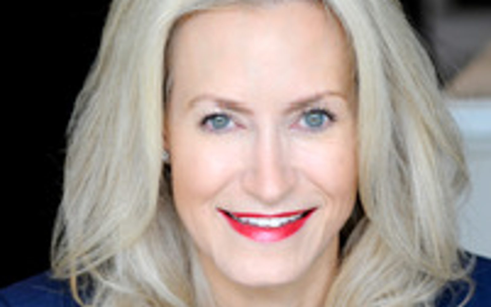 Woman with long blond hair wearing a blue dress and pearls. 