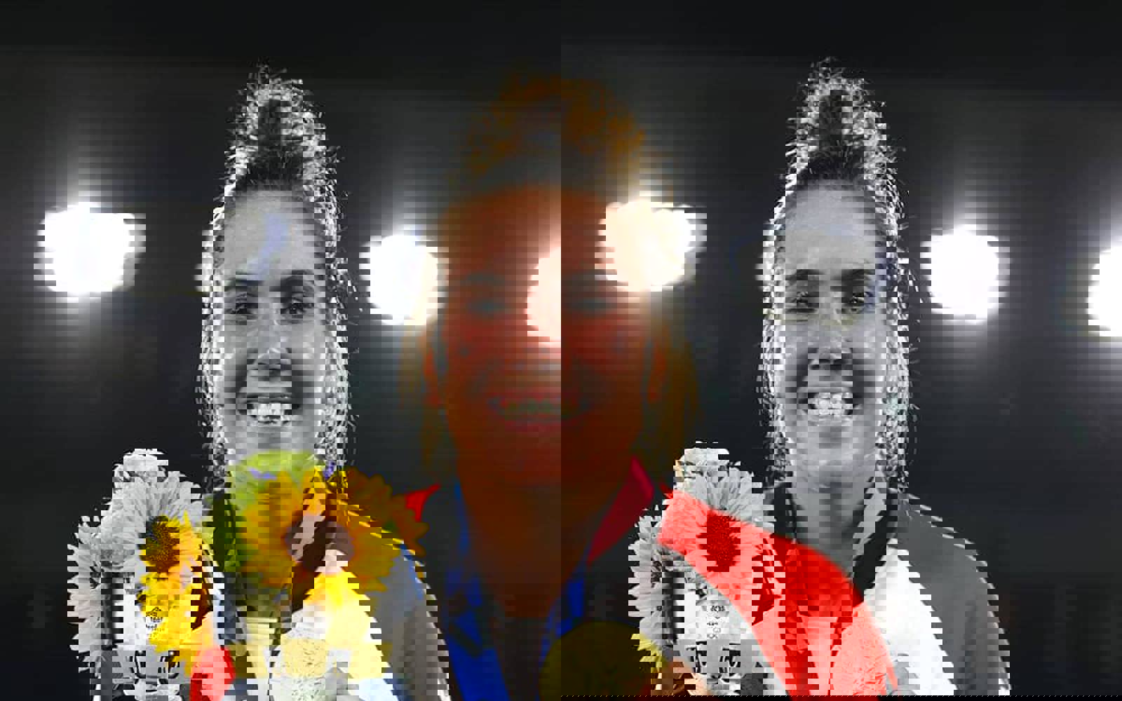 Headshot of a woman with hair in a topknot. She is wearing a Team Canada zip up and holding a bouquet of sunflowers. Around her neck is a gold medal. 