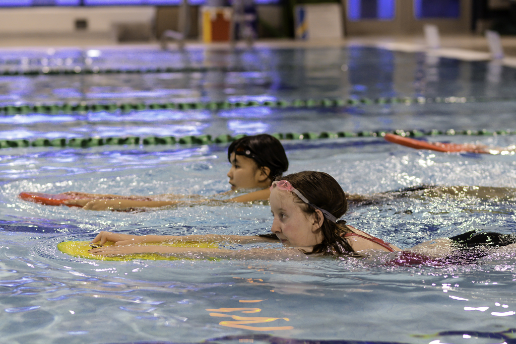 Two athletes swimming in a pool. They are holding on to kick boards and swimming across the pool.