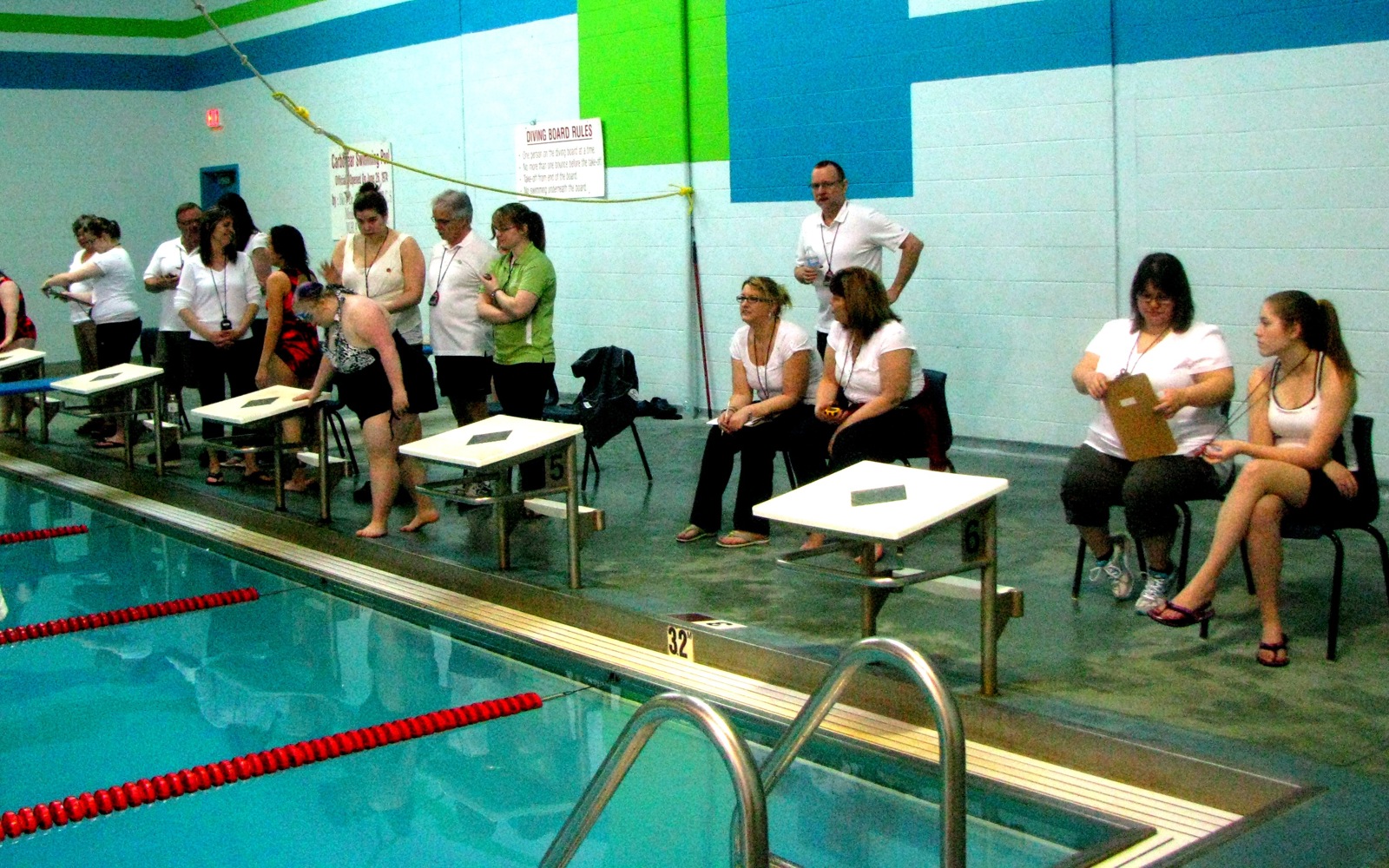 Multiple volunteers in white t-shirts are sitting next to a swimming pool preparing for a match.