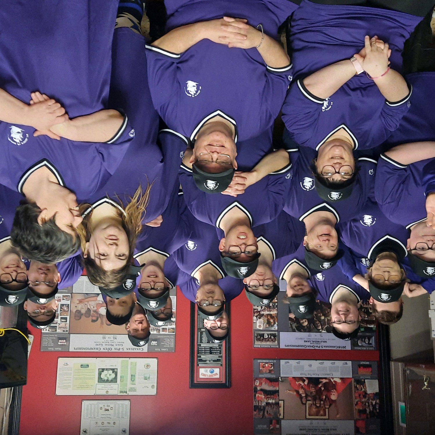 A group photo where everyone is wearing matching purple jerseys. There are 5 rows of people of mixed genders and ages, and everyone is smiling for the camera.