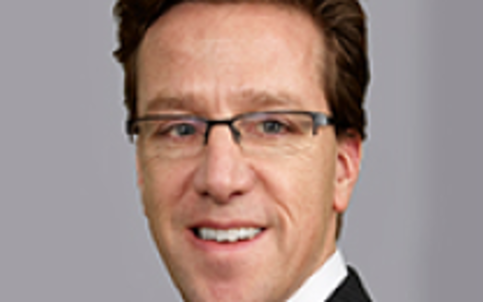 Man in black suit with white shirt and dark hair smiling at the camera. 
