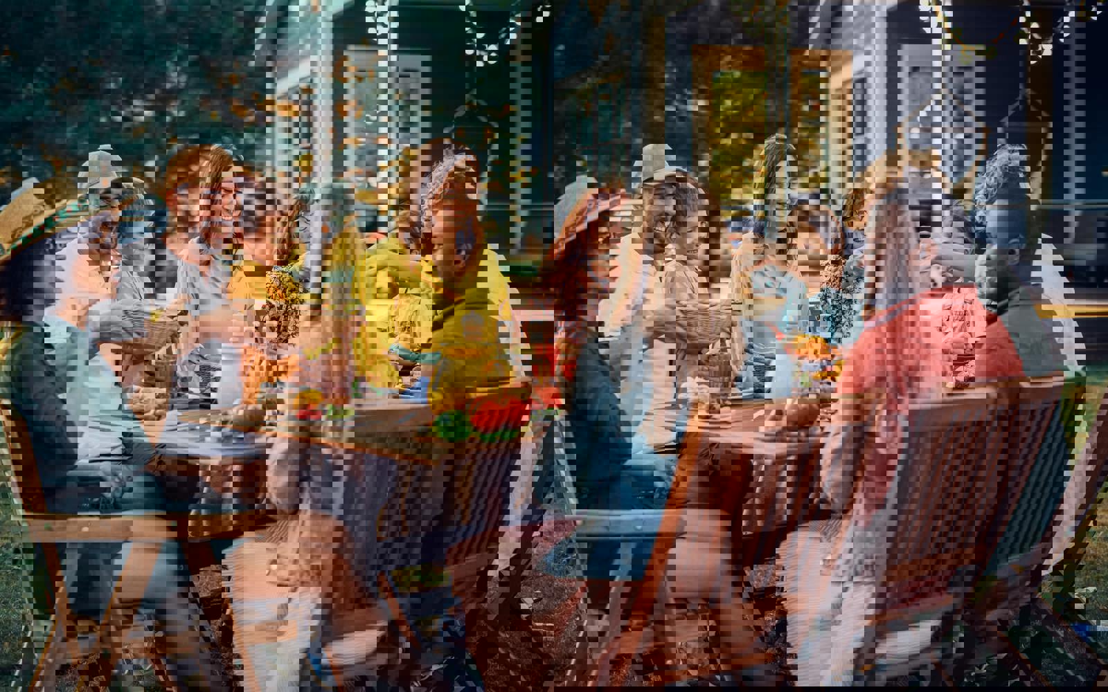 Group of people sitting outside at a picnic table, with table covered in food and drinks. 