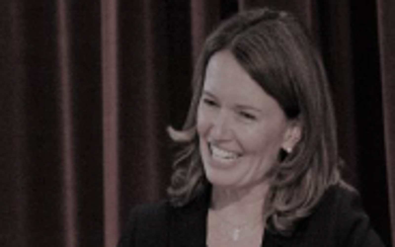 Woman with long dark hair and wearing black sweater smiling at camera. 