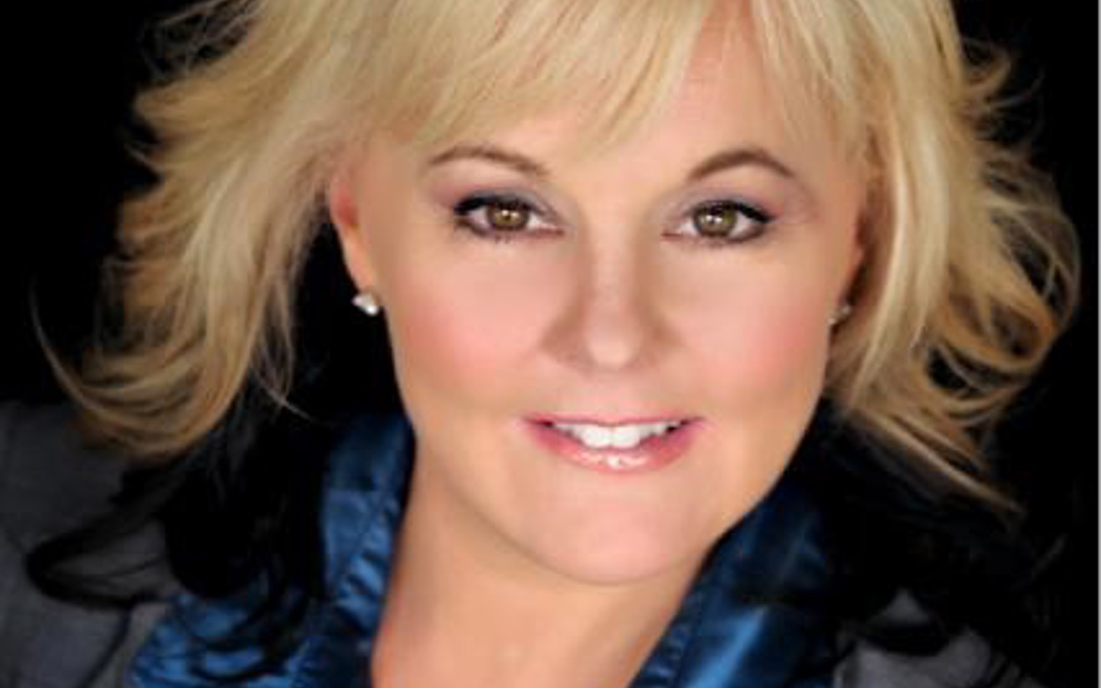 Headshot of a woman with blond hair in a grey suit jacket and blue shirt. 