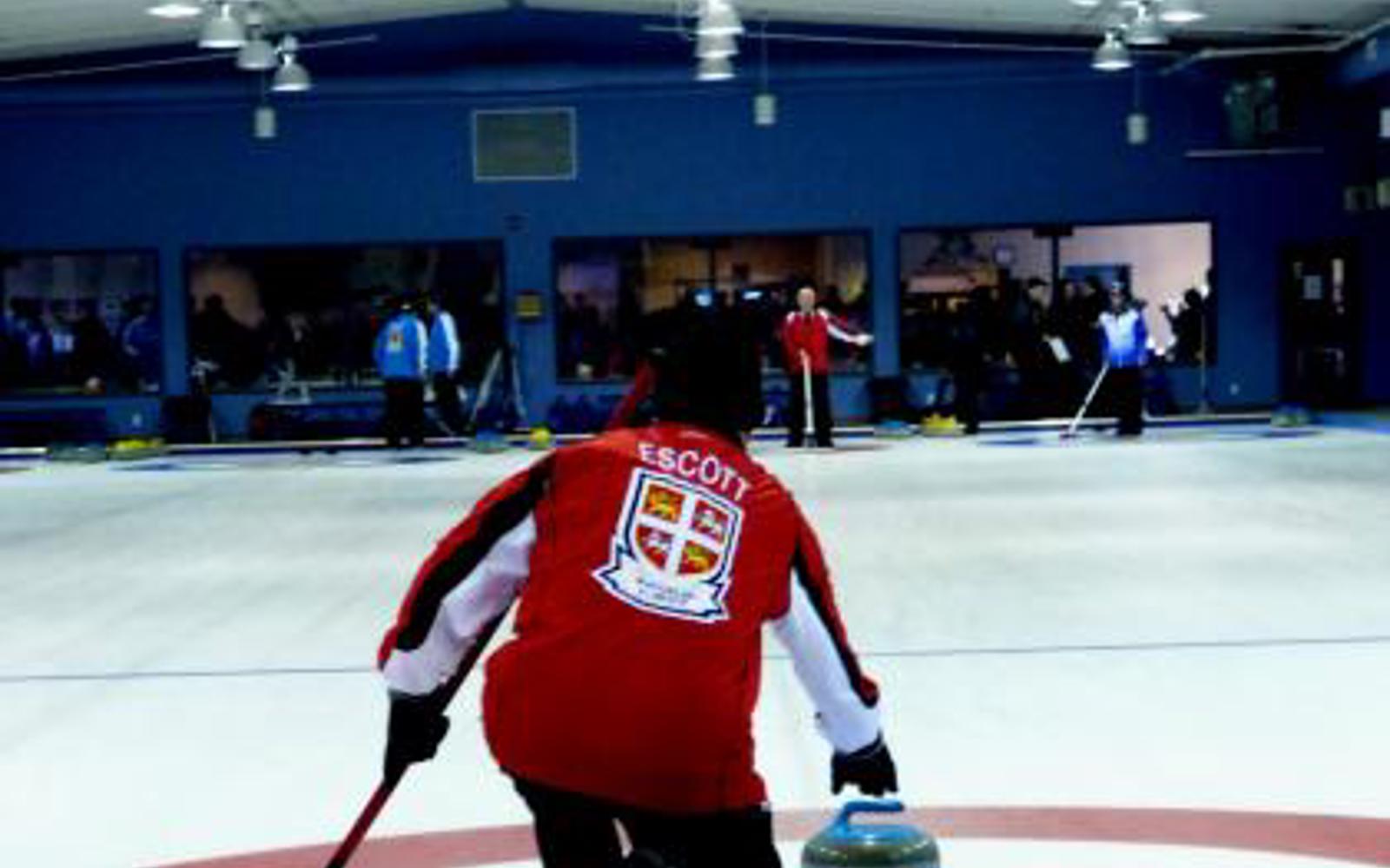 Man in a Newfoundland and Labrador jersey about to throw a curling stone on a curling rink 