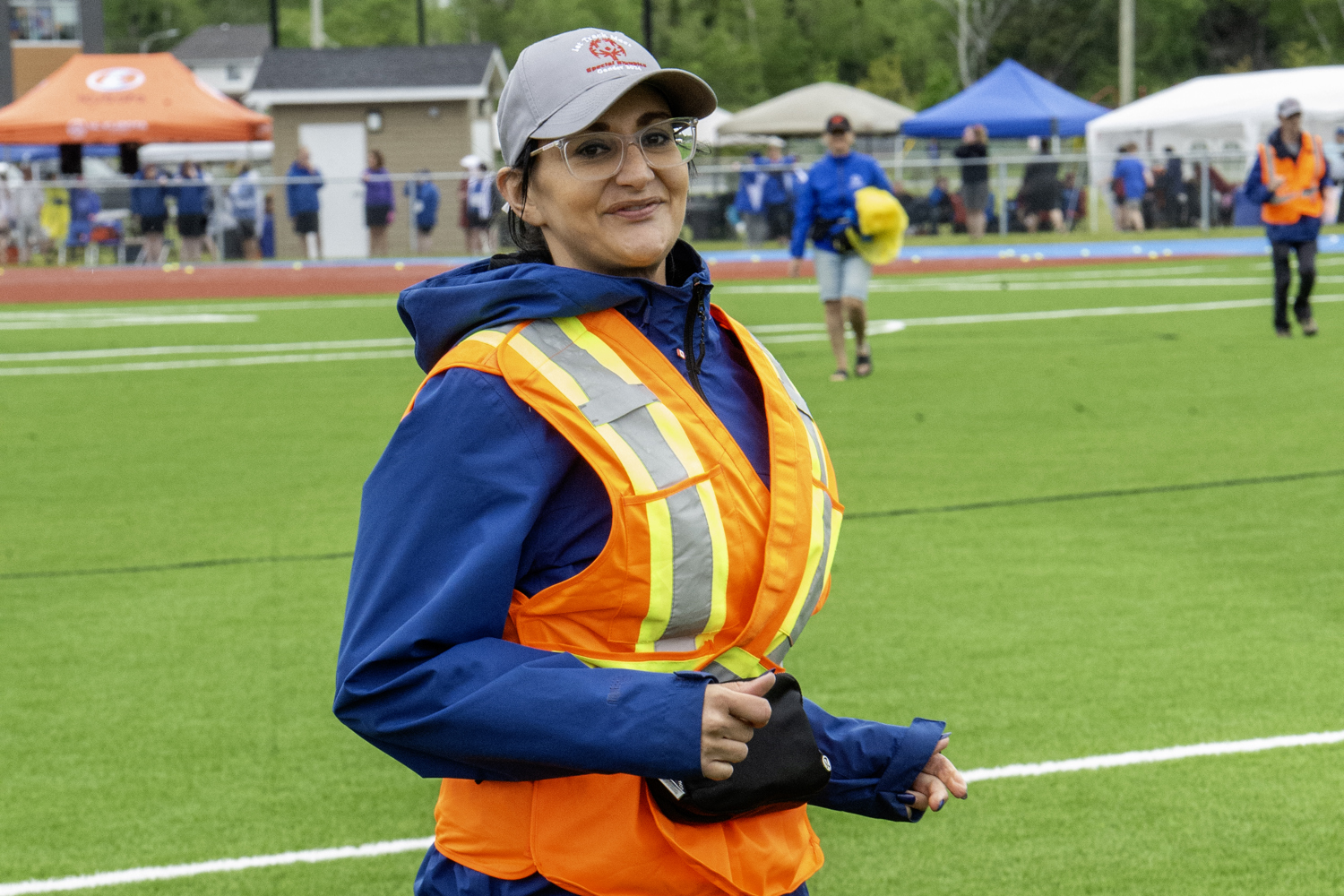 A photo of a volunteer mid run, wearing a bright orange and yellow safety vest, and a Special Olympics Newfoundland & Labrador grey baseball cap.