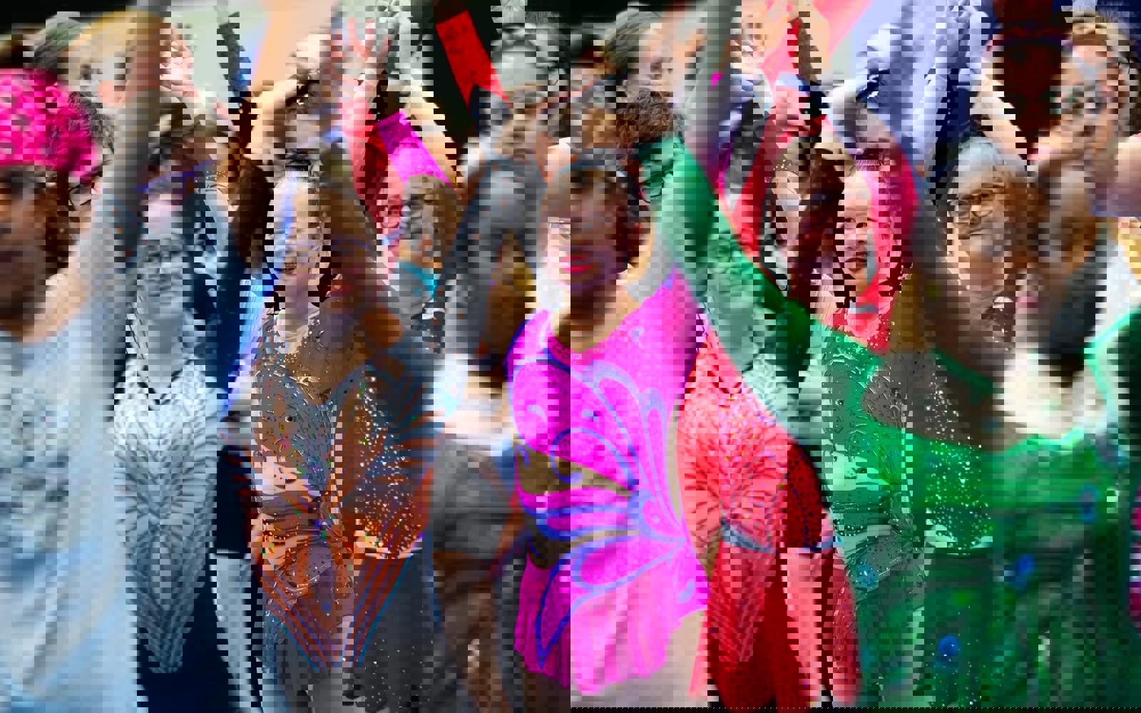 Group of athletes with arms in the air. All are smiling and wearing figure skating costumes 