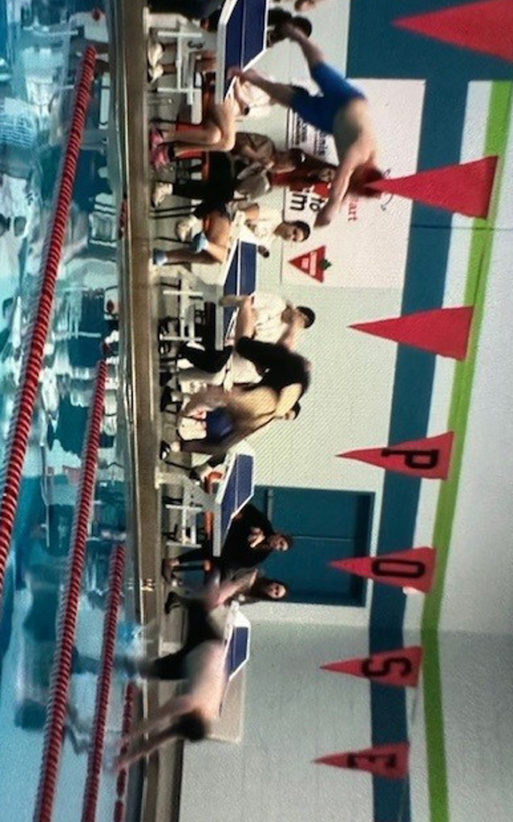 Three Special Olympics Newfoundland & Labrador athletes are diving into an indoor swimming pool from the diving blocks at the edge of the pool. The three athletes are blurry due to being in motion.