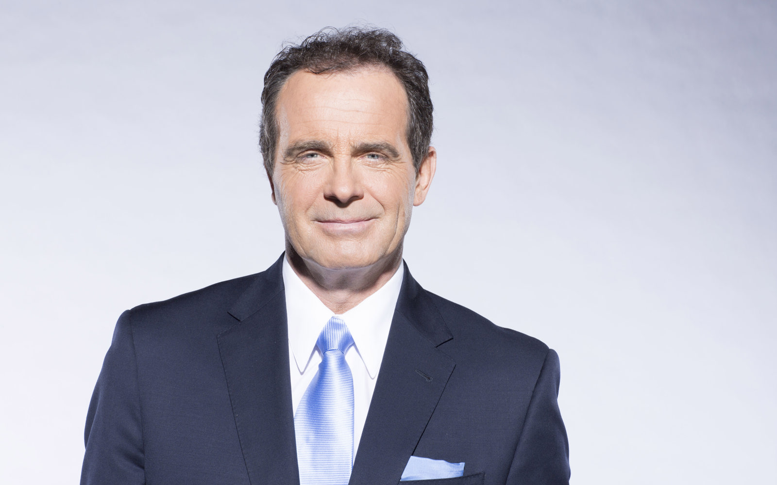 Headshot of a man with dark hair wearing a blue suit, white shirt and blue tie. 