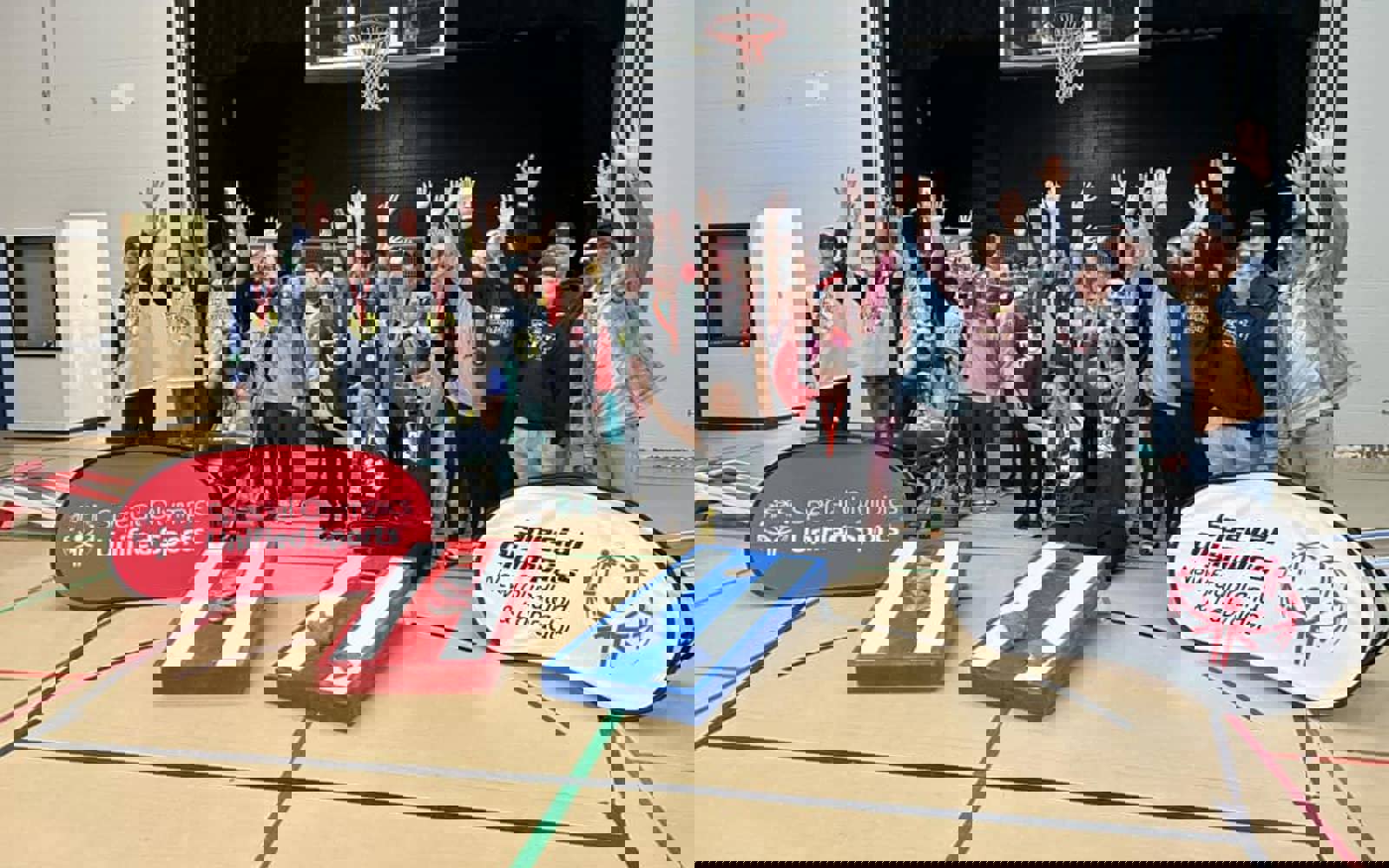 Diverse group of people in a gym. In front of them is two cornhole games. 