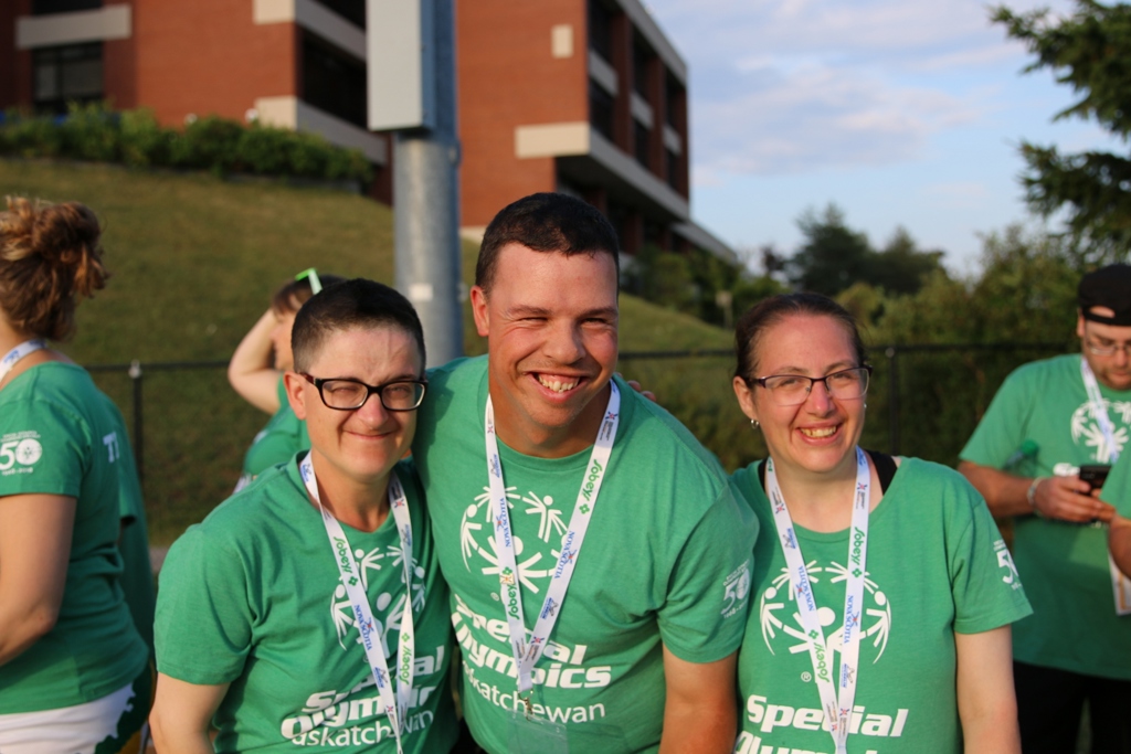 Three Special Olympics Saskatchewan athletes are smiling for the camera. They are all wearing green Special Olympics Saskatchewan t-shirts and white lanyards.