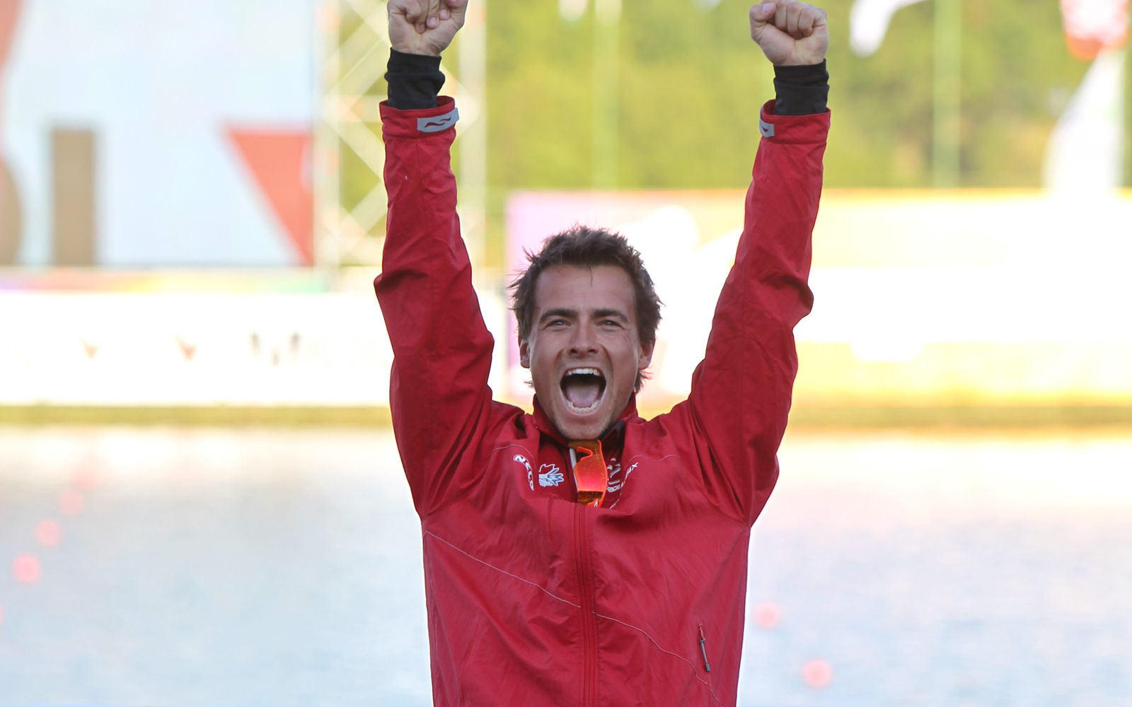 Man in red coat and black pants with his arms in the air cheering. 